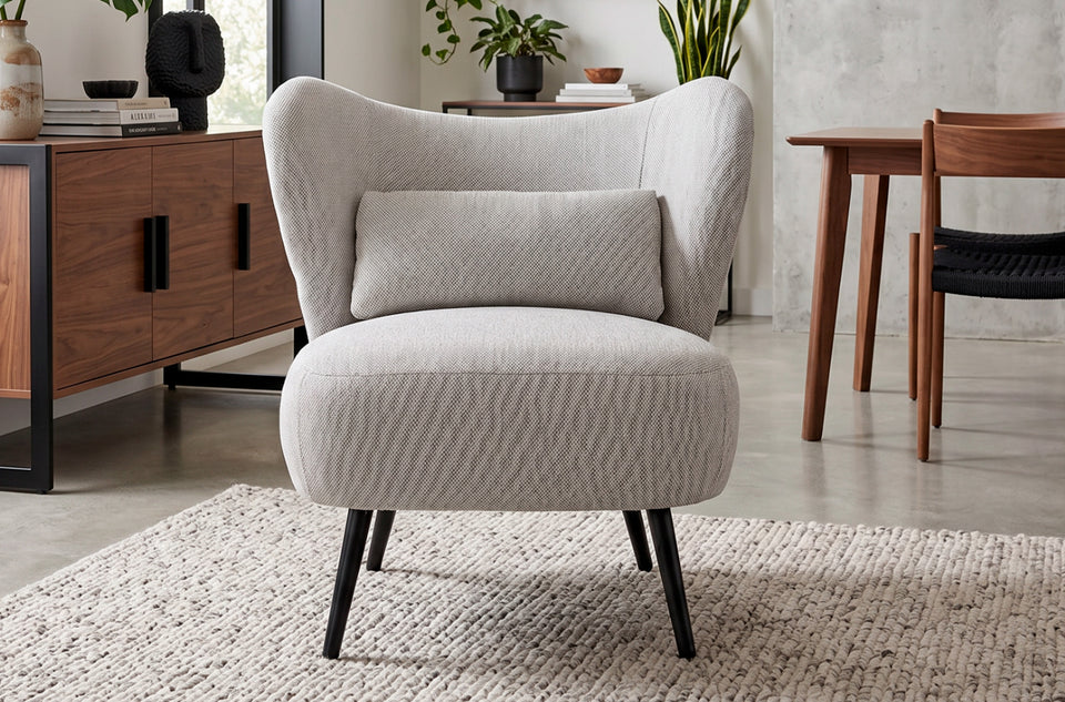 Fauteuil rembourré Elle gris chiné dans un salon, près d'un buffet et d'une table, sur un tapis